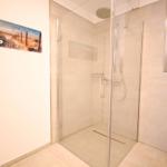 Dusche mit Glaswand, Toilette und Wandbild mit Strandmotiv.