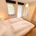 Doppelbett mit weißer Bettwäsche, Kleiderschrank und Fenster mit Blick auf Grün.