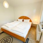 Schlafzimmer mit Holzbett, weißen Laken und Fenster mit Vorhängen.