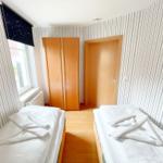 Zwei Betten mit weißen Laken und Handtüchern, Wand mit Streifen, Fenster und Tür.