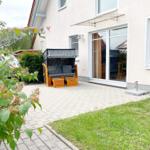 Hinterhof mit Holzliege, Pflaster und Grünfläche. Glastür führt ins Haus.