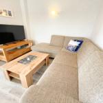 Wohnzimmer mit Ecksofa, Holztisch und Fernseher auf Holzregal.