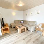 Wohnzimmer mit Sofa, Couchtisch und Stuhl. Holzboden und -decke. Wandbilder.