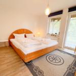 Schlafzimmer mit Holzbett, Fenster und Tür. Teppich mit Kompassmuster.