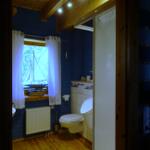 Badezimmer mit blauen Wänden, Toilette und Fenster mit Segelbootmodell.