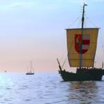 Historisches Segelschiff mit Wappen segelt auf ruhigem Meer. Im Hintergrund ist ein kleiner Segelboot sichtbar.
