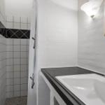 Bad mit Dusche, Waschbecken und Spiegel an der Wand.