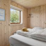 Schlafzimmer mit Holzwand, Bett und Fenster mit Blick auf Bäume.