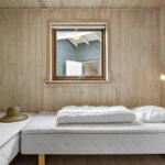 Schlafzimmer mit Holzwand, Bett und Fenster. Hut liegt auf Matratze.