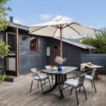Terrasse mit Tisch, Stühlen und Sonnenschirm vor einem Holzhaus.