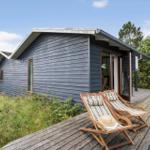 Holzterrasse mit zwei Liegestühlen vor einem grauen Holzhaus mit Glastür.