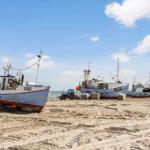 Fischerboote liegen auf dem Strand, ein Traktor steht daneben.