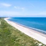 Haus am Strand mit Dünen und blauem Meer im Hintergrund.