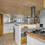 Küche mit Holzboden, -decke und -schränken. Esstisch, Herd und Dunstabzug.