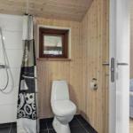 Badezimmer mit Dusche, Toilette und kleinem Fenster. Tür führt in Schlafzimmer mit Bett.