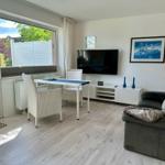 Wohn- und Essbereich mit Sofa, TV und Tisch. Große Fenster mit Blick auf Garten.