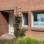 Rotes Backsteinhaus mit Eingang, Fenster und Rosenstrauß.