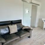 Ein Wohnzimmer mit Ledersofa, weiße Sitzgelegenheit und Glaswand.