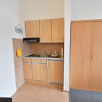 Küche mit Holzschränken, Spüle und Dunstabzug. Nebenraum mit Kleiderschrank.