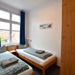 Zwei Einzelbetten mit Bettwäsche, Fenster mit blauen Vorhängen und Holzwand.