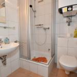 Badezimmer mit Dusche, Waschbecken und Toilette. Orange Handtuch liegt in der Dusche.