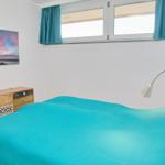 Schlafzimmer mit Bett, Schrank und Fenster mit Vorhängen.