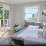 Ein Wohnzimmer mit Sofa, Balkon und Meerblick durch Fenster.