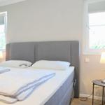 Schlafzimmer mit Bett, zwei Fenstern und Nachttischen mit Lampen.