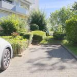 Pflasterweg führt zu einer Wohnung mit Garten und Parkplatz. Ein weißes Auto steht bereit.