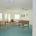 Großer Raum mit Tisch, Stühlen und Tischfußball. Blaues Teppichboden und Fenster.