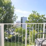Terrasse mit Sitzgelegenheit und Blick auf Grünflächen und Gebäude.