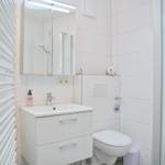 Badezimmer mit Waschbecken, Toilette und Dusche. Weiße Fliesen und Spiegelschrank.