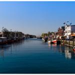 Hafen mit Booten und Steg, Gebäude entlang des Wassers.