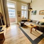 Wohnzimmer mit Sofa, Couchtisch und Fernseher. Fenster mit Blick auf Balkon.