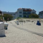 Sandy beach path with wooden walkway, beach chairs, and buildings in background.