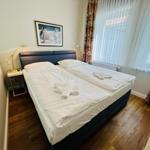 Doppelbett mit weißen Bettwäsche, Holzboden und Fenster mit Vorhängen.