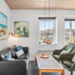 Wohnzimmer mit Sofa, zwei Sesseln und Tisch. Fenster und Glastür zeigen Blick auf Wasser.