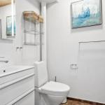 Badezimmer mit Waschbecken, Toilette und Dusche. Wandbild und Spiegel sichtbar.