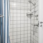 Duschkabine mit weißen Fliesen und blau-weißem Vorhang.