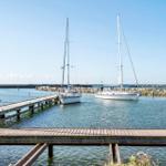 Hafen mit zwei Segelyachten und hölzernem Steg im Hintergrund.