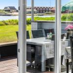 Terrasse mit Tisch, Stühlen und Blick auf Wasser und Grünflächen.