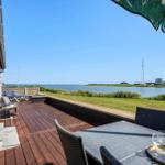 Terrasse mit Sitzgelegenheiten und Blick auf Wasser und Grasland.