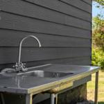 Außenwaschbecken mit Armatur an grauer Holzhauswand