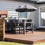 Terrasse mit Tisch, Stühlen und Sonnenschirm. Holzgeländer und Vogelhaus sichtbar.