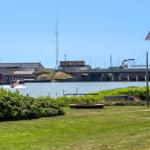 Grüner Rasenbereich mit Blick auf Wasser, Brücke und rote Gebäude.