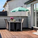 Terrasse mit Tisch, Stühlen und grünem Sonnenschirm. Holzdecke und Glasfassade sichtbar.