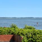 Ein Stand-up-Paddler auf einem See mit Windkraftanlagen am Horizont.