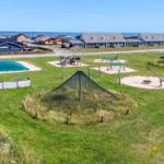 Grüner Spielplatz mit Sandkisten, Rutsche und Klettergerüsten. Hintergrund: Ferienhäuser und Meer.