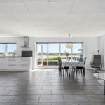 Offener Raum mit Küche, Esstisch und Sofa. Große Fenster mit Blick auf Wasser.