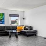 Schwarzes Ledersofa mit orangefarbenen Kissen, Glas-Tisch und Wandbild mit Segelschiff.